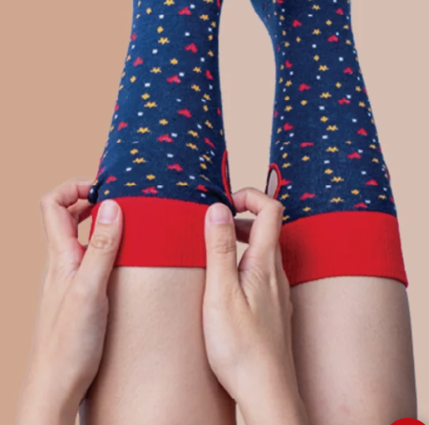 Red and navy star and heart socks shown being pulled on using the hole at the cuff